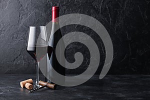 Elegant glass and bottle of red wine with corks and corkscrew on black stone background. Natural Light