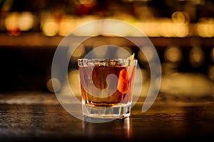 Elegant glass filled with strong cocktail with whiskey on the bar against the lights