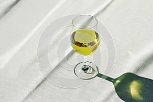 An elegant glass of green cannabis wine on a table with soft green fabric. Sunlight dances through, casting gentle shadows and