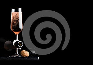 Elegant glass of pink rose champagne with cork and wire cage and bottle on black marble board on black background. Space for text