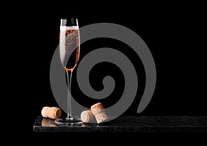 Elegant glass of pink rose champagne with corks on black marble board on black background.