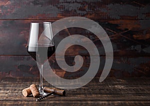 Elegant glass of red wine with corks and corkscrew on dark wooden background. Natural Light