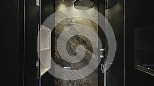 Elegant glass shower with amazing wall made of natural stone ceramic tiles equipped with white shelves and cozy lighting