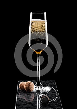 Elegant glass of yellow champagne with cork and wire cage on black marble board on black background