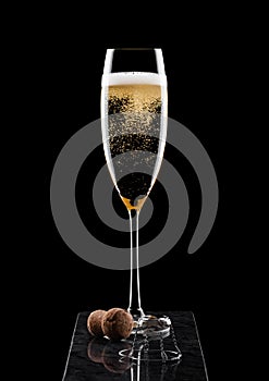 Elegant glass of yellow champagne with cork and wire cage on black marble board on black background