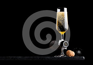Elegant glass of yellow champagne with cork and wire cage and bottle on black marble board on black background. Space for text