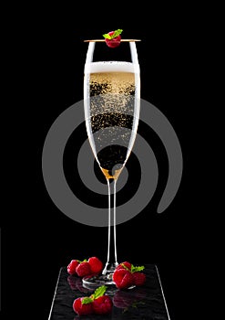 Elegant glass of yellow champagne with rasspbery and fresh berries with mint leaf on stick on black marble board on black