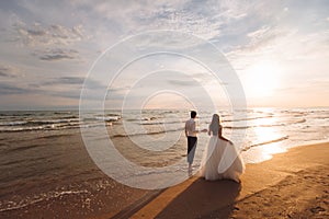 Elegant gorgeous bride and groom walking on ocean beach during sunset time. Romantic walk newlyweds on tropical island
