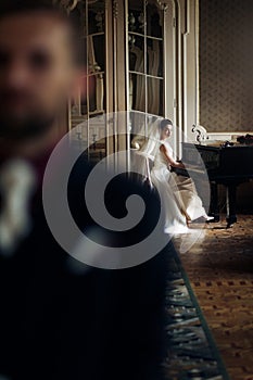 elegant gorgeous bride playing the fortepiano and stylish handsome groom posing in rich old room. sensual look. unusual luxury we photo