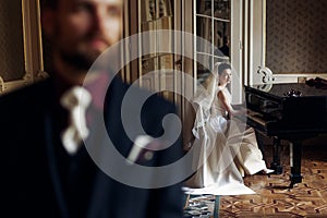 elegant gorgeous bride playing the fortepiano and stylish handsome groom posing in rich old room. sensual look. unusual luxury we