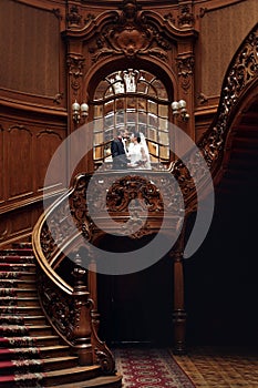 elegant gorgeous bride and stylish groom hugging, romantic moment. standing on wooden stairs in rich room. unusual wedding couple