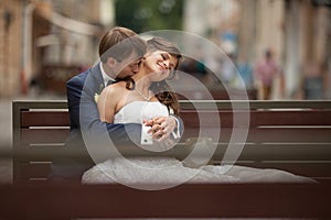 Elegant gorgeous happy bride and groom sitting on a bench on the