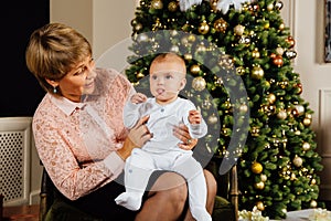 Elegant grandmother with a child in her arms on the background of a Christmas tree.