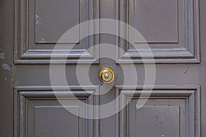 Elegant gray color painted wooden door surface with relief frames and round vintage knob in center. Details of Paris door.