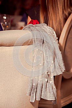 Elegant gray women`s clothing with white beads slung across the back of a beige chair