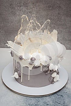 Elegant grey cake with modern design. Caramel, waffle paper, french meringues and white chocolate decoration