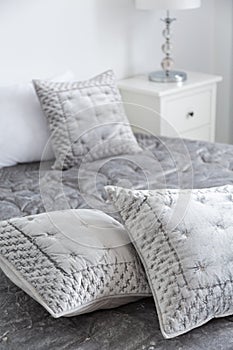 Elegant grey pillows on bed in minimal hotel bedroom interior with lamp on white cabinet. Real photo