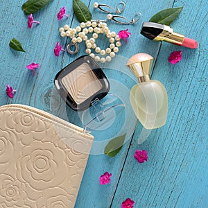 Elegant handbag,cosmetics powder, lipstick perfume, pearl necklace and earrings on a blue background. View from above