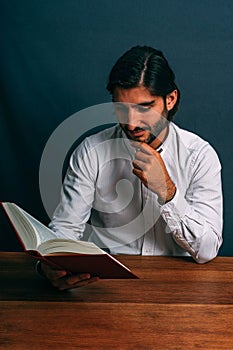 Elegante Hispano hombre lectura pensativamente sobre el de madera mesa un libro 