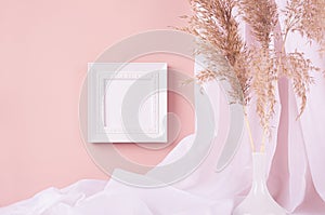 Elegant home decoration - square blank photo frame hanging on pink wall, curtain, beige fluffy reeds in vase. Contemporary simple.