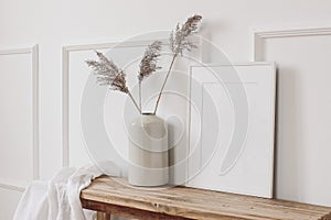 Elegant home interior decor still life photo. Vase with dry reed, grass on old wooden bench. Blank white picture frame