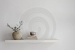 Elegant home still life. Floating shelf. Textured vase with green olive tree branches and old books. Cup of coffee, tea