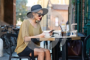 Elegant Italian woman with hat and glasses writes a message with her smartphone
