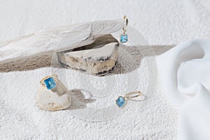 Elegant jewellery set of gold earrings and ring with blue topaz on white background with stones and wood. Minimal style