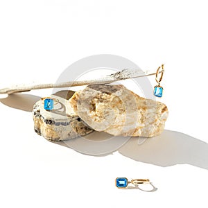 Elegant jewellery set of golden ring andearrings with blue topaz on white background with stones and wood. Minimal style