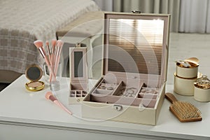 Elegant jewelry box with beautiful bijouterie and cosmetics on dressing table in bedroom