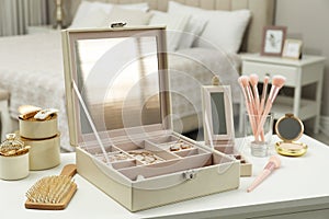 Elegant jewelry box with beautiful bijouterie and cosmetics on dressing table in bedroom