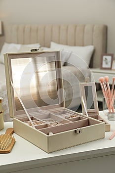 Elegant jewelry box with beautiful bijouterie and cosmetics on dressing table in bedroom