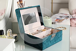 Elegant jewelry box with beautiful bijouterie, cosmetics and perfume on dressing table in room
