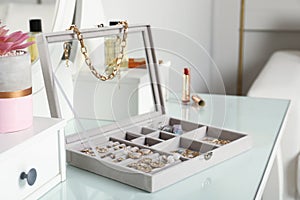 Elegant jewelry box with beautiful bijouterie, cosmetics and stylish accessories on dressing table in room