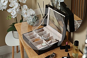 Elegant jewelry box with beautiful bijouterie, cosmetics and stylish accessories on dressing table in room