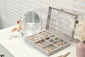 Elegant jewelry box with beautiful bijouterie and makeup products on dressing table indoors