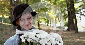 Elegant lady in hat with bouquet of flowers smiling, looking at camera in park