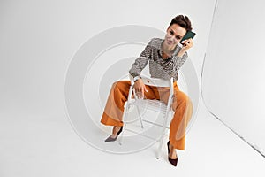 Elegant lady with a short haircut in classic pants and a shirt posing sitting on a chair on a white background