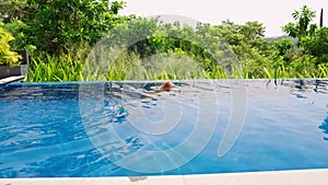 Elegant lady swims in infinity pool at tropical villa. Leisure in high-end resort with jungle view. Relaxing luxury