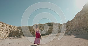 Elegant lady walking with violin and bow on desert at cliff under bright sky