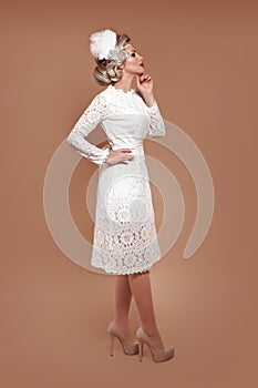 Elegant lady in wedding white dress with retro hairstyle posing isolated on studio beige background. Beautiful blonde bride woman