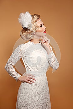 Elegant lady in wedding white dress with retro hairstyle posing isolated on studio beige background. Beautiful blonde bride woman