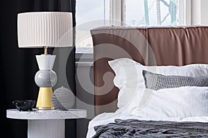 Elegant lamp on bedside table next to cozy bed