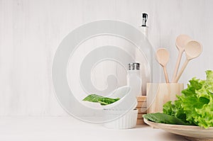 Elegant light kitchen interior with wooden utensils, ceramics and green leaves greens on white wood shelf.