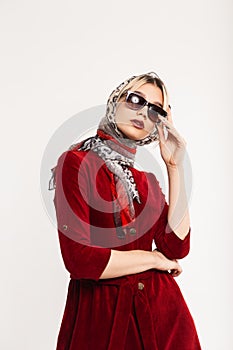 Elegant lovely young woman with sexy lips in fashionable sunglasses in red dress in leopard headscarf poses near vintage wall in