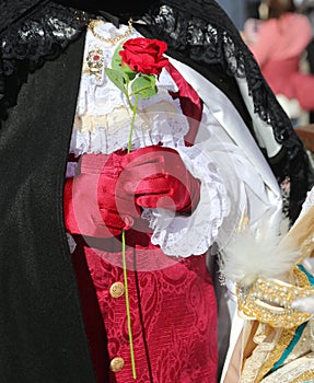elegant lover with red rose in hand and ceremonial dress awaits his woman during the masquerade ball