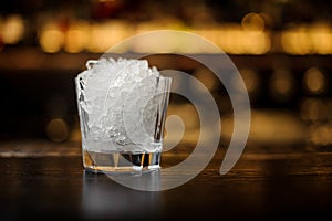 Elegant low cocktail glass filled with ice cubes on the bar counter of restaurant