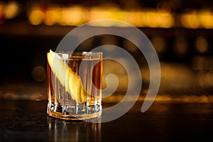 Elegant low glass filled with strong cocktail with light whiskey on the bar against the lights