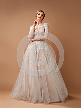 Elegant lush wedding dress.  Blonde model in white lace wedding gown and long sleeves. Full-length portrait of young smiling bride