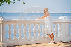 Elegant luxurious woman in white dress enjoying the view of the sunset on seaside promenade